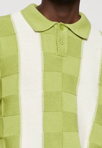Groene en witte geblokte polo met een gebreide textuur, voorzien van een kraag en knoopsluiting, en contrasterende kleurvlakken.