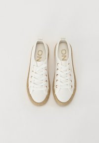 Hvite lerrets sneakers med en vevd jute såle, med metalliske snørehull og en løkke på hælen. Gulllogo på innersålen.
