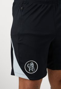 Sorte atletiske shorts med lyseblå sidelomme, der har en tekstureret kvalitet, elastisk talje og et rundt logo med en løve og initialer.