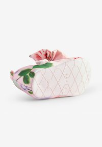 Zapato floral tipo slip-on de tela rosa con hojas verdes y patrones de rosas, con una suela blanca texturizada que presenta un patrón de diamantes.