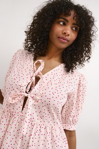 Helles rosa Kleid mit kleinen, verstreuten, dunkelrosa Herzmustern, einem V-Ausschnitt mit Ribbons zur Bindung und puffärmeligen kurzen Ärmeln.