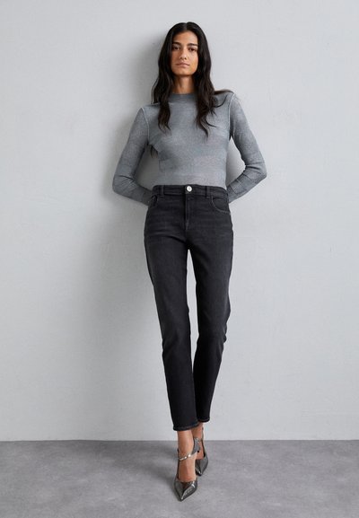 Top gris de manga larga combinado con jeans negros de tiro alto y zapatos de tacón metálicos, presentando una silueta ajustada y una textura suave.