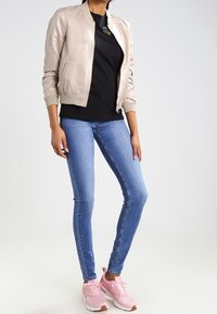 Světlý béžový bomber, černé tričko, modré úzké džíny a růžové tenisky s bílou podrážkou. Jednoduchý design a přiléhavý střih.