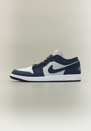 Nízkoprofilová tenisová obuv Nike z bielej a tmavomodrej kože s čiernymi šnúrkami a logom Nike Swoosh na neutrálnej pozadí.