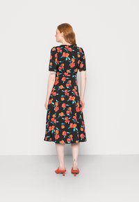 Vestido preto de flores com mangas curtas, apresentando flores vermelhas e azuis e saia godê. Combinado com saltos vermelhos, visto de trás.
