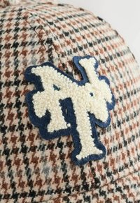 Håndsyet kasket i houndstooth mønster lavet af beige, brun og sort uld med et tekstureret hvidt og blåt broderet logo. Den har en buet skygge og syede detaljer.