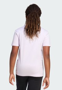 Jasnofioletowa bawełniana koszulka z krótkim rękawem, okrągłym dekoltem i gładką teksturą, widoczna z tyłu. Poniżej noszone są czarne spodnie.