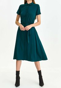 Teal kortärmad klänning med krage, åtsittande midja och utsvängd kjol; har en framsida med knappslå och en knytning i midjan.