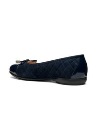 Chaussure plate bleu marine avec une texture en daim matelassé, dotée d'un embout brillant et d'un nœud décoratif à l'avant. Vue de côté.