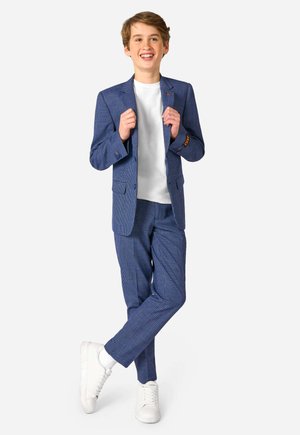 Costume à carreaux bleus avec une coupe ajustée, t-shirt blanc en dessous et baskets blanches. Présente un subtil accent orange sur la manche.