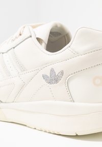 Baskets en cuir blanc avec des coutures discrètes, une finition texturée et un logo brodé en argent sur le côté.