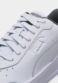 Λευκό δερμάτινο αθλητικό παπούτσι Puma με κορδόνια, ανάγλυφο λογότυπο Puma και μαύρη εσωτερική επένδυση, σε κοντινή λήψη.