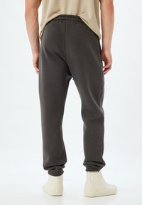 Donkergrijze joggers met een elastische tailleband, taps toelopende benen en ribbelboorden. Draag ze met witte high-top sneakers. Soepele stoftextuur.
