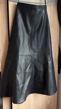 Black faux leather A-line skirt hanging on blue hanger against wood wardrobe background.