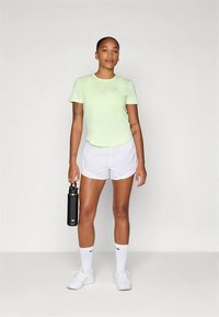 Hele-rohelise lühikeste varrukatega T-särk valgete lühikeste pükstega, valgete sokkide ja valgete tossudega. Käes must joogipudel. Minimalistlik disain.