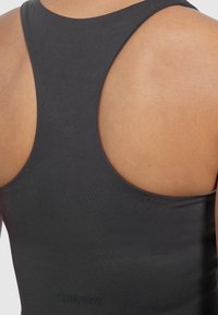 Zwarte racerback tanktop met een gladde textuur. Heeft een lage ruglijn en de merknaam in reliëf op de taille in een contrasterend materiaal.