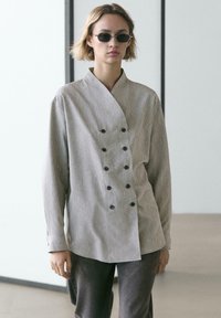 Gestreiftes Hemd zum Knöpfen aus grauem und weißem Baumwollstoff, mit zweireihigem Schnitt und Schalkragen. Kombiniert mit dunkler Hose.