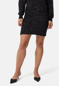 Abito nero con paillettes caratterizzato da maniche lunghe, polsini a coste e una silhouette aderente. Abbinato a décolleté nere a punta con accenti in tessuto.