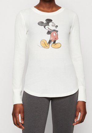 Person wearing a white long-sleeve shirt with a classic walking Mickey Mouse graphic and dark gray pants.