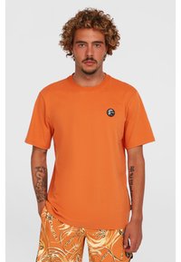 Orange bomulds t-shirt med korte ærmer, rund hals, med et lille sort cirkulært logo på venstre bryst. Glat tekstur.