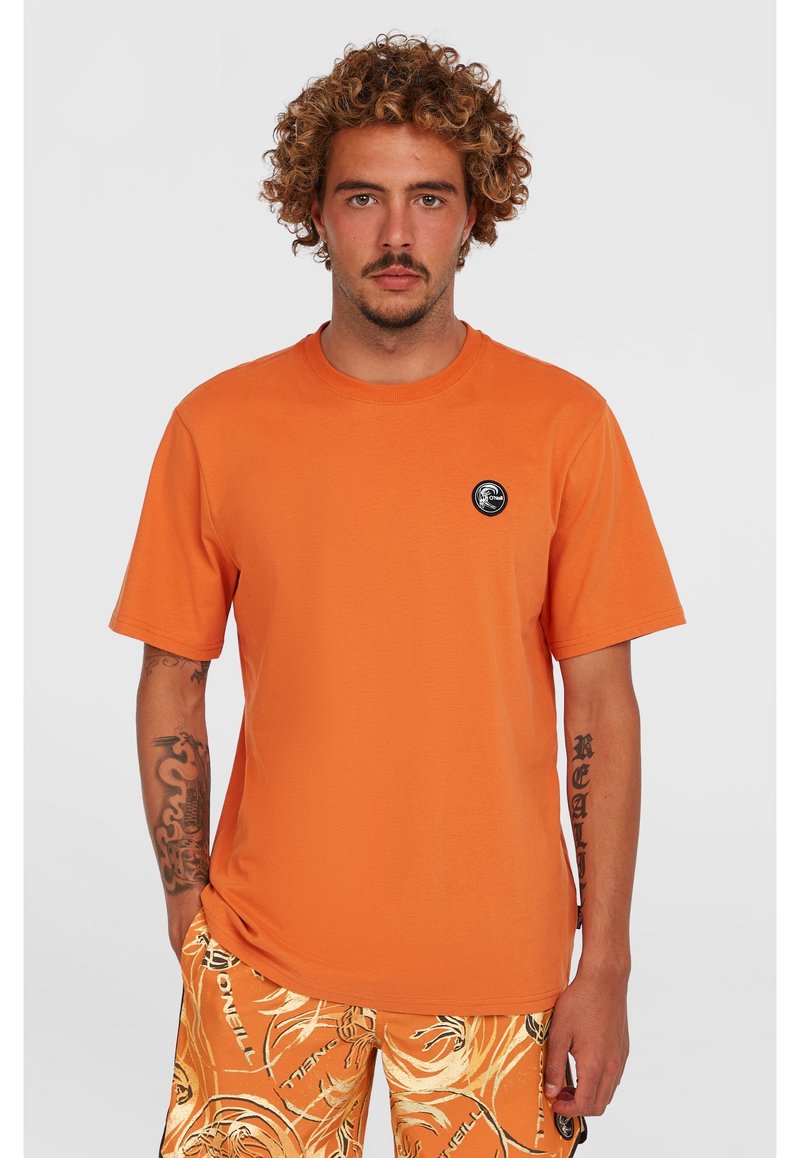 Orange bomulds t-shirt med korte ærmer, rund hals, med et lille sort cirkulært logo på venstre bryst. Glat tekstur.