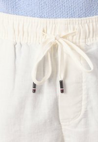 Shorts albe din in cu talie adunată, având un șnur cu accente negre și roșii. Textură netedă și buzunare laterale vizibile.