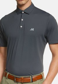 Dunkelgraues Poloshirt mit klassischem Kragen, Knopfleiste mit drei Knöpfen und dezentem Logo auf der linken Brust. Der Stoff wirkt glatt und leicht.