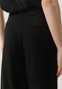 Pantalon noir ajusté avec une légère texture, doté de deux poches arrière et d'une ceinture standard.