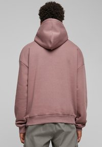 Sudadera con capucha rosa, de corte relajado, con puños y dobladillo acanalados, textura suave y una capucha grande, vista desde la parte de atrás.