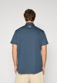 Marineblå polo shirt med korte ærmer, krave og et broderet logo på ryggen. Glat tekstur med en lige kant.