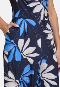 Tuta navy con grande motivo floreale blu e bianco; presenta un tessuto liscio, gamba larga e tasche laterali.