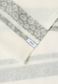 Kermanvärinen kangas, jossa on harmaa eläinkuosisomiste reunassa, taitettuna niin, että reunan lähellä näkyy pieni valkoinen "CECIL"-etiketti.