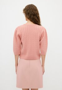 Pull en maille rose avec des manches trois-quarts, texture douce et ourlet côtelé, associé à une jupe assortie d'une teinte similaire.