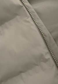 Bežinė paklota medžiaga su lygiu paviršiumi ir metaliniu užtrauktuku, esantį siūlėje. Minimalistinis dizainas pabrėžia elegantišką išvaizdą.