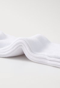 Calze bianche di cotone disposte con una consistenza morbida, polsini a coste e una finitura liscia, che mostrano un design semplice e funzionale.