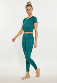 Sada aktivního oblečení v odstínu teal, obsahující krátký rukáv a crop top s vysokým pasem a legíny. Hladká textura, přiléhavý střih a elastický materiál.