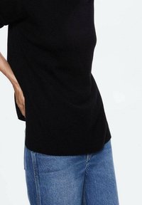 Maglione nero a maglia con una vestibilità comoda, maniche corte e orlo arrotondato, abbinato a jeans di denim blu chiaro con un taglio classico.