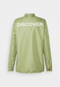 Lysegrøn jakke med lange ærmer, der har ordet "DISCOVER" i fede hvide bogstaver på ryggen. Glat tekstur, krave-design.