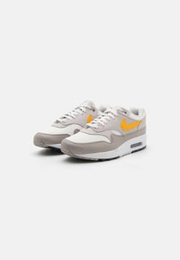 Grå og hvide sportsko med en overdel i mesh og læder, der har en orange Nike swoosh, tyk hvid sål og tekstureret sort ydersål.