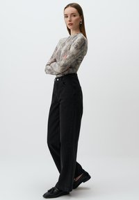 Maglietta aderente a maniche lunghe in grigio e beige con un motivo astratto, abbinata a jeans neri a gamba larga a vita alta e scarpe nere basse.