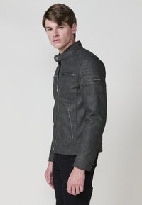 Giubbotto da moto grigio in ecopelle con accenti trapuntati sulle spalle, due tasche sul petto con zip e una tasca inferiore con zip, design attillato.