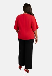 Blusa rossa a maniche corte con zip sul retro, abbinata a pantaloni neri a gamba larga e sandali alti rossi. Tessuto liscio, vestibilità rilassata.