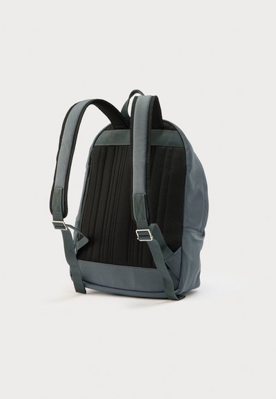 Γκρι και μαύρο σακίδιο με υφασμάτινη πλάτη με υφή από δίχτυ, μαξιλαρωμένους ιμάντες ώμου και ρυθμιζόμενα κλιπ. Ο αεροδυναμικός σχεδιασμός τονίζει τη λειτουργικότητα.