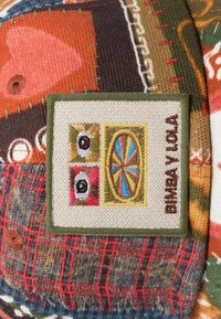 Gorra multicolor con un tejido texturizado y un parche. El parche presenta ojos bordados y un diseño circular, etiquetado como "BIMBA Y LOLA".