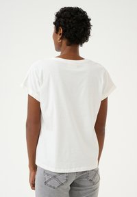 T-shirt en coton blanc avec des manches courtes roulées, une coupe décontractée et un col en scoop, associé à un jean en denim gris avec des coutures sur les poches arrière.