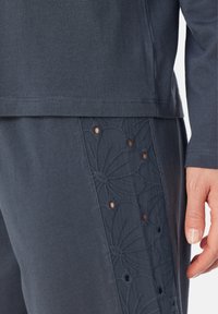 Mörkgrå lounge-set som innehåller en mjuk T-shirt och byxor. Byxorna har broderad blommönster med utskärningar längs sidan.