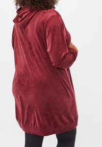 Bordeauxfarbener Hoodie mit weichem, plüschigem Material und langen Ärmeln. Verfügt über einen Kordelzug an der Kapuze und einen gestrafften Saum für eine lockere Passform.