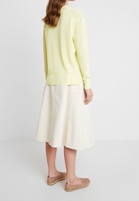 Jasnożółty sweter na drutach o prążkowanej fakturze, połączony z kremową spódnicą w kształcie litery A. Stylizację dopełniają brązowe buty wsuwane.