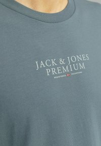 Katoenen T-shirt in gedempt blauw, met een ronde hals, korte mouwen en witte bedrukte tekst "JACK & JONES PREMIUM" op de voorkant.