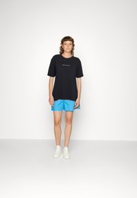 Black oversized t-shirt with a white text graphic, paired with light blue shorts, and white sneakers. Simple design and casual fit.
